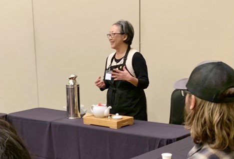 photograph of a woman wearing apron behind a table with a tea set